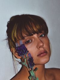 Close-up portrait of woman with flowers against wall