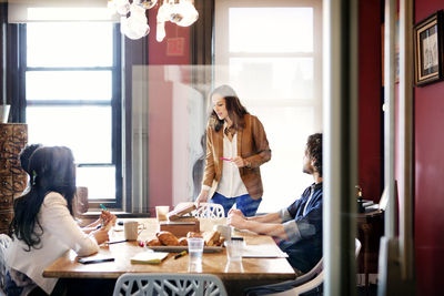 Woman explaining business people during meeting in office seen through glass