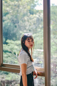 Side view of young woman standing against window