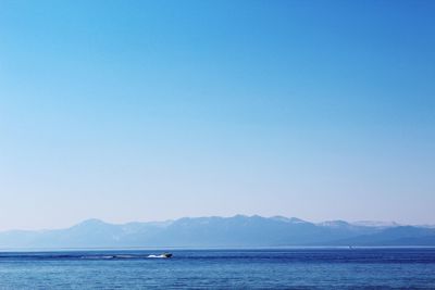 Scenic view of sea by mountains against clear blue sky