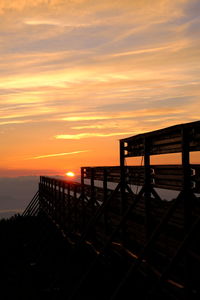 Silhouette railing by sea against orange sky