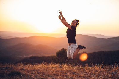 Man with arms raised on field against sky during sunset