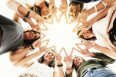 Portrait of happy friends joining fingers against clear sky