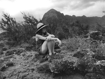 Rear view of woman sitting on rock against sky