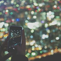 Midsection of person photographing illuminated mobile phone at night