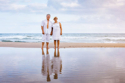 Portrait of romantic senior couple standing at beach against sky