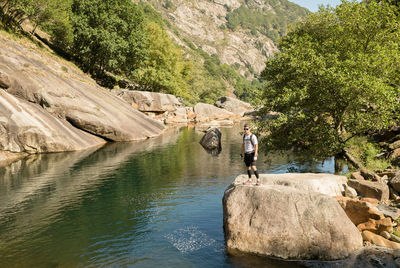 Full length of man standing on rock by river in forest