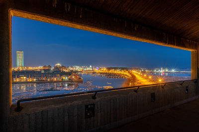 Illuminated bridge over river by buildings against sky at dusk