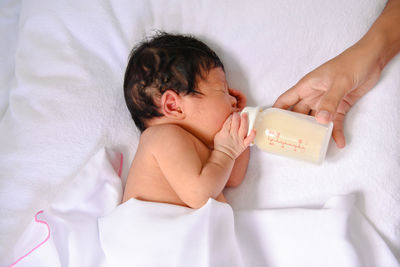Cropped hand of woman feeding milk to baby girl with bottle on bed