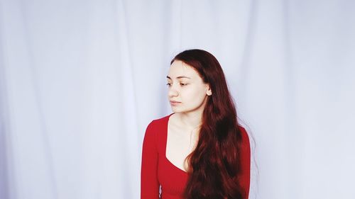 Young woman looking away while standing against wall