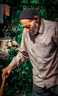 Midsection of man holding hat standing against plants