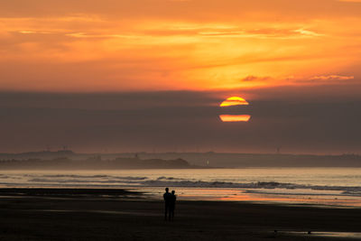 Silhouette people standing at beach against sky during sunset