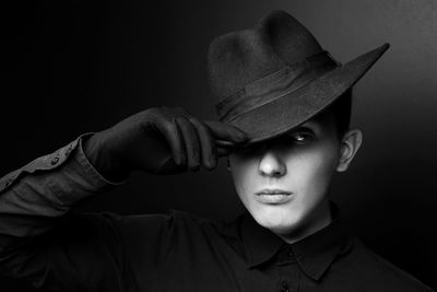 Young man wearing hat looking away against black background