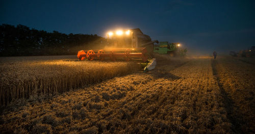 Machine harvesting crops on field at dusk