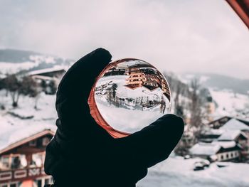 Person hand holding snow covered mountain against sky