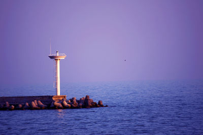 Lighthouse by sea against clear sky