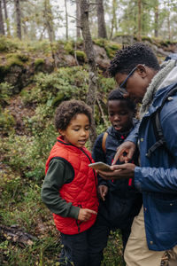 Father showing smart phone to sons while hiking in forest
