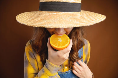Portrait of woman wearing hat against orange background
