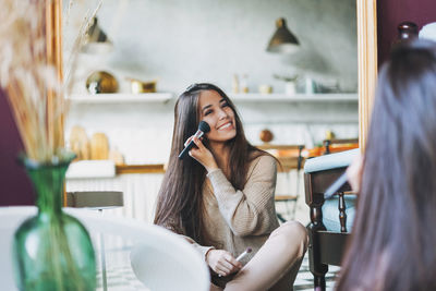 Young woman using phone while sitting in laptop