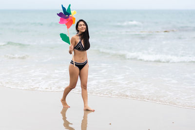 Full length of woman holding pinwheel toy while walking at beach