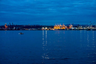 Illuminated city by sea against sky at dusk