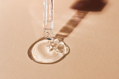 A drop of skin moisturizing serum flowing from a pipette on a beige neutral background close-up.