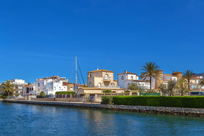 Buildings by sea against clear blue sky