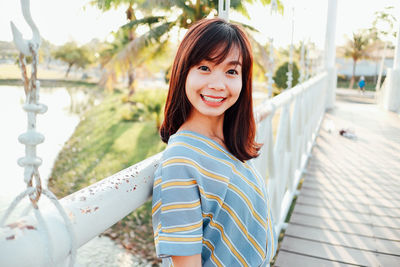 Portrait of smiling young woman standing on footbridge