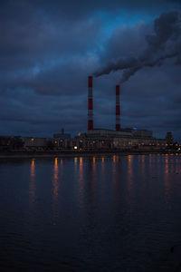 Smoke emitting from factory by river at dusk
