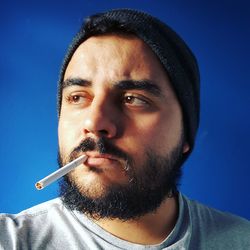 Close-up of man smoking against blue background