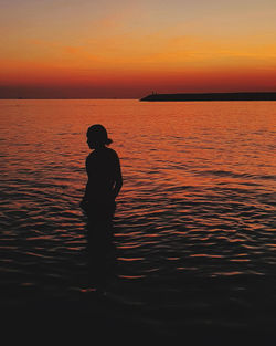 Silhouette man standing in sea against sky during sunset