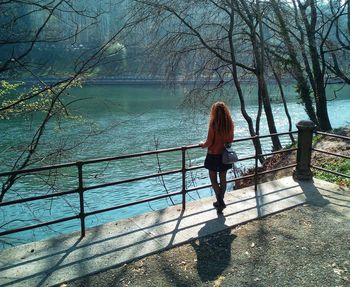 Rear view of woman standing by railing against trees