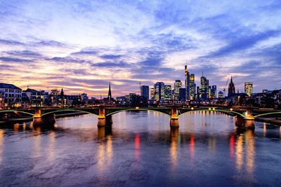 Illuminated bridge over river in city against sky at sunset