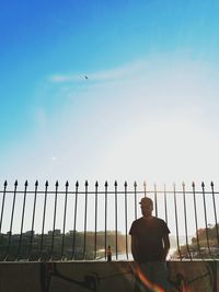 Man standing by fence against sky on sunny day