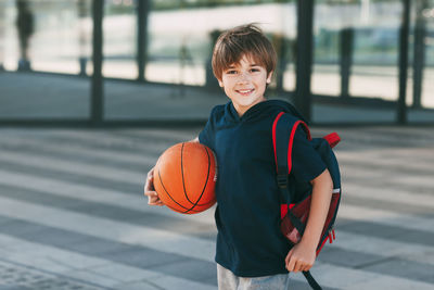 Portrait of a beautiful boy in sports uniform with a backpack and a basketball. the boy smiles