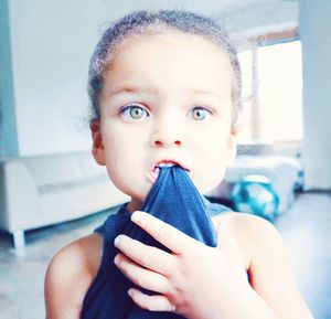 Portrait of cute girl biting fabric at home