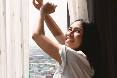 Close-up of smiling young woman standing by window at home