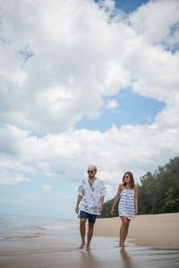 Man and woman walking at beach against sky