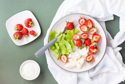 Fresh whole and sliced strawberries, cottage cheese and lettuce on a plate and sour cream in a bowl