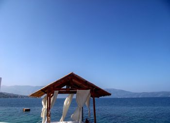 Lifeguard hut by sea against clear blue sky