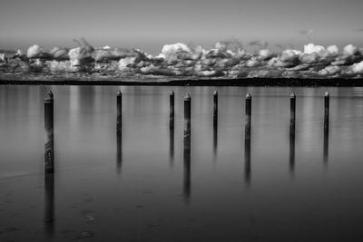 Wooden posts in lake against sky