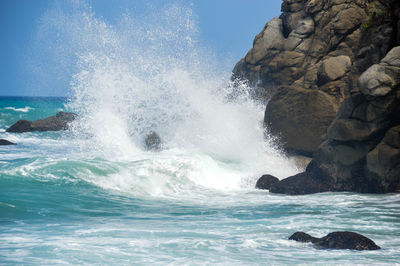 Waves splashing on rock formation against sky