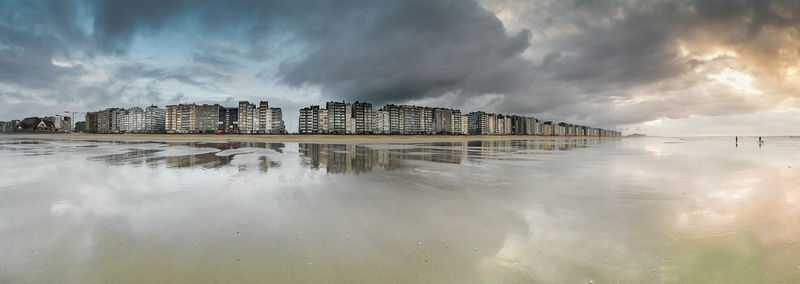 Reflection of buildings in river against cloudy sky at dusk