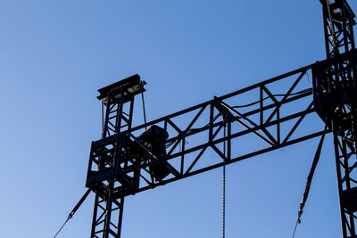 Low angle view of silhouette crane against clear blue sky