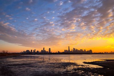 Silhouette buildings by city against sky during sunset