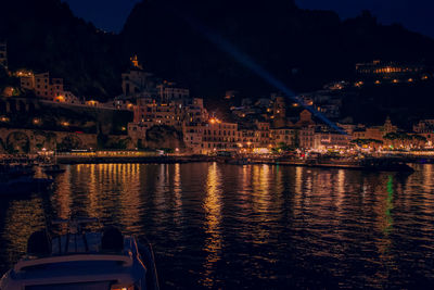 Illuminated city by river against sky at night