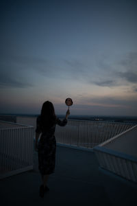 Rear view of woman holding hand mirror against sky during sunset