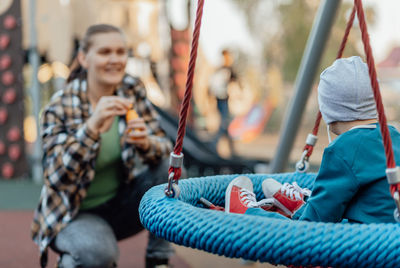 Cute little boy with in a funny hat walks in the playground with his mother, spinning on a carousel