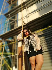 Low angle view of woman standing by scaffolding and cordon tape against built structure