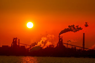 Silhouette smoke emitting from factory against sky during sunset